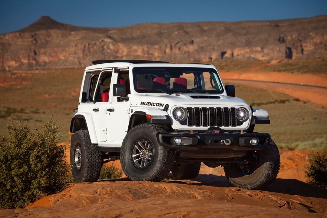 Front 3/4 view of white 2024 Jeep Wrangler Rubicon parked in a desert.