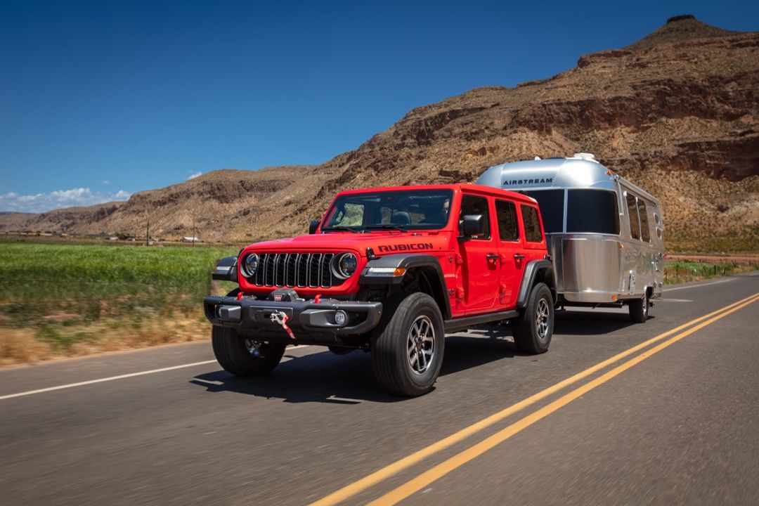 Front 3/4 view of a 2025 Jeep Wrangler towing a camper.