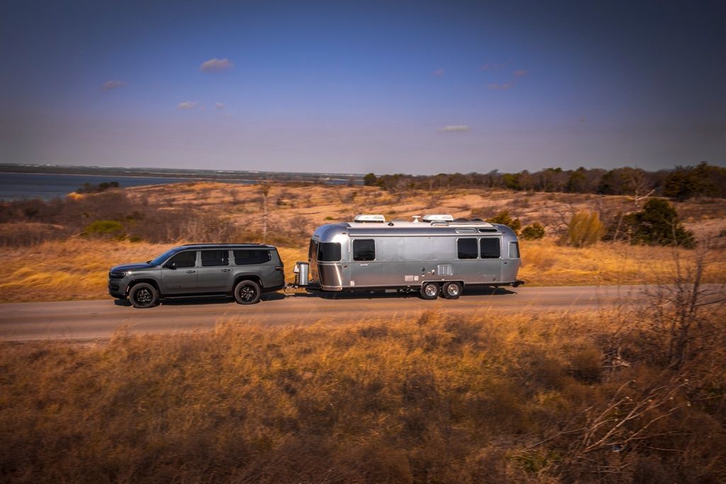 Vue latérale du VUS Jeep Wagoneer L 2024 remorquant une roulotte sur une route.