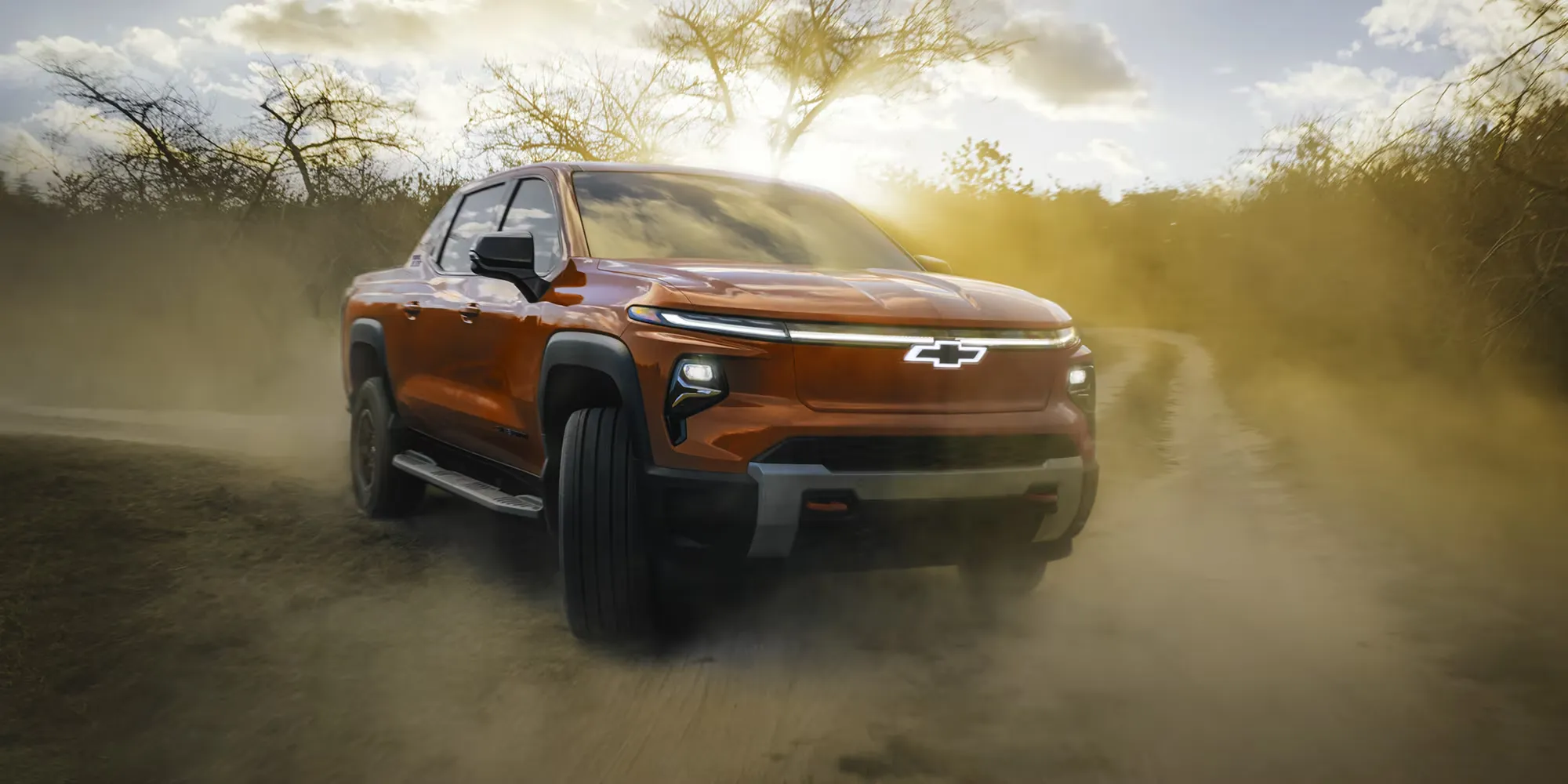 Orange Chevrolet Silverado EV driving off-road on a dusty trail.