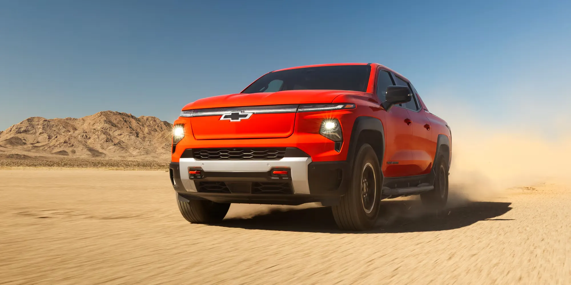 Orange Chevrolet Silverado EV driving through the desert with a modern design.