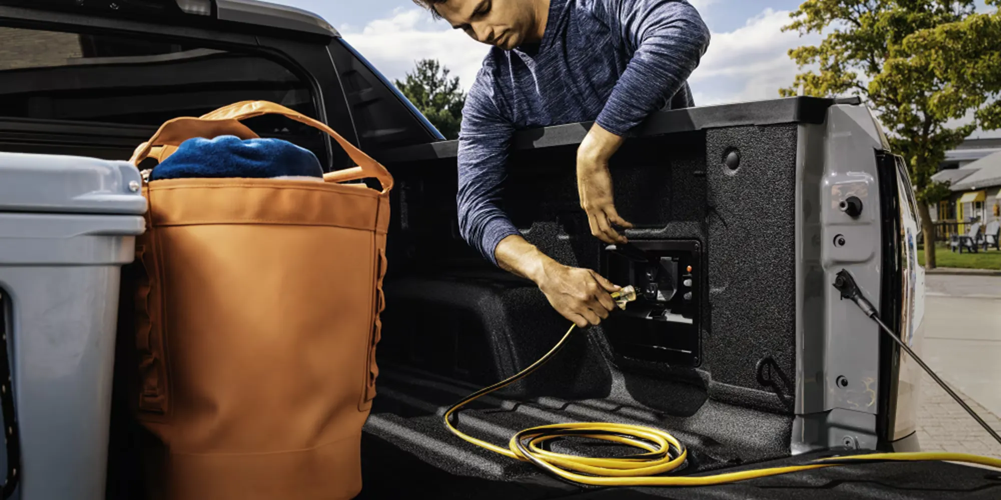 User plugging an accessory into the bed of a Chevrolet electric pickup.