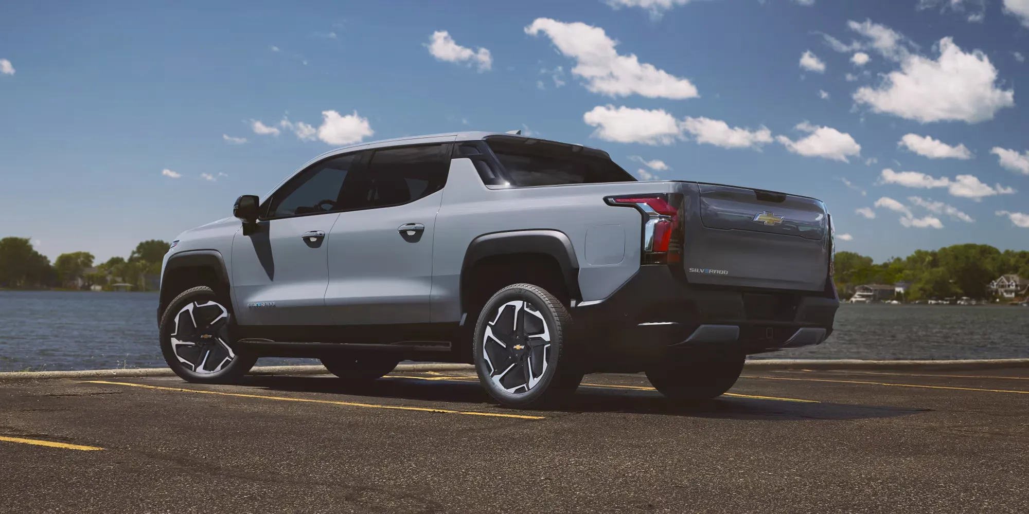 Grey Chevrolet Silverado EV parked by a lake under a blue sky.
