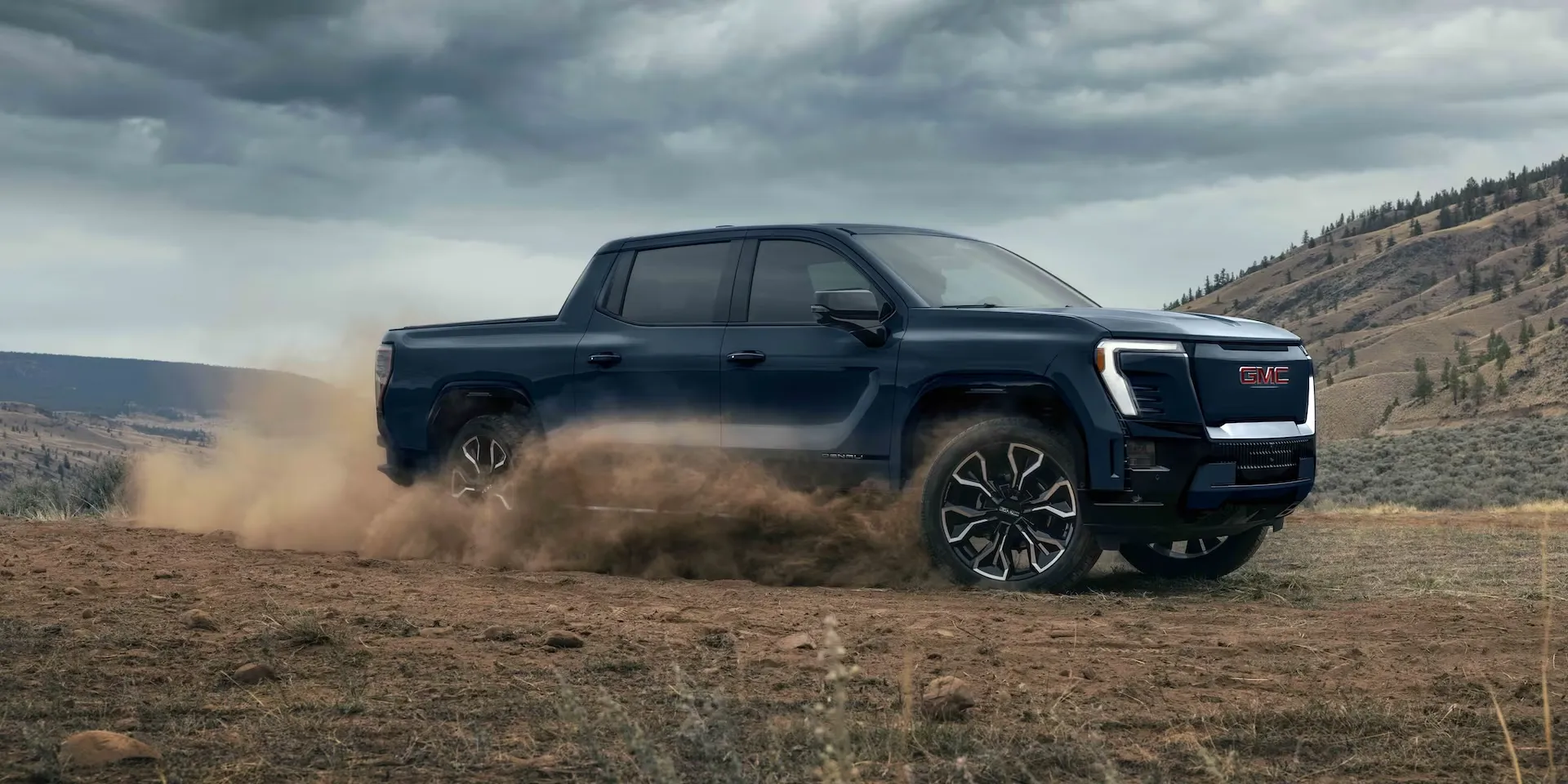 Blue 2026 GMC Sierra EV driving over rough terrain.