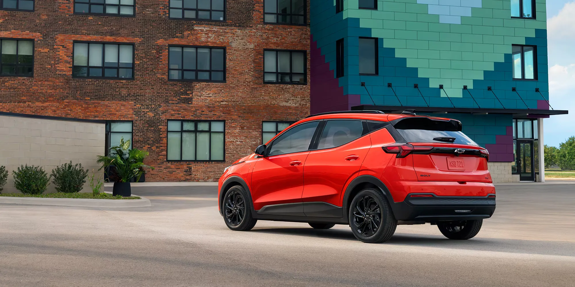 Chevrolet Bolt 2027 rouge stationn&eacute;e devant un immeuble en brique.