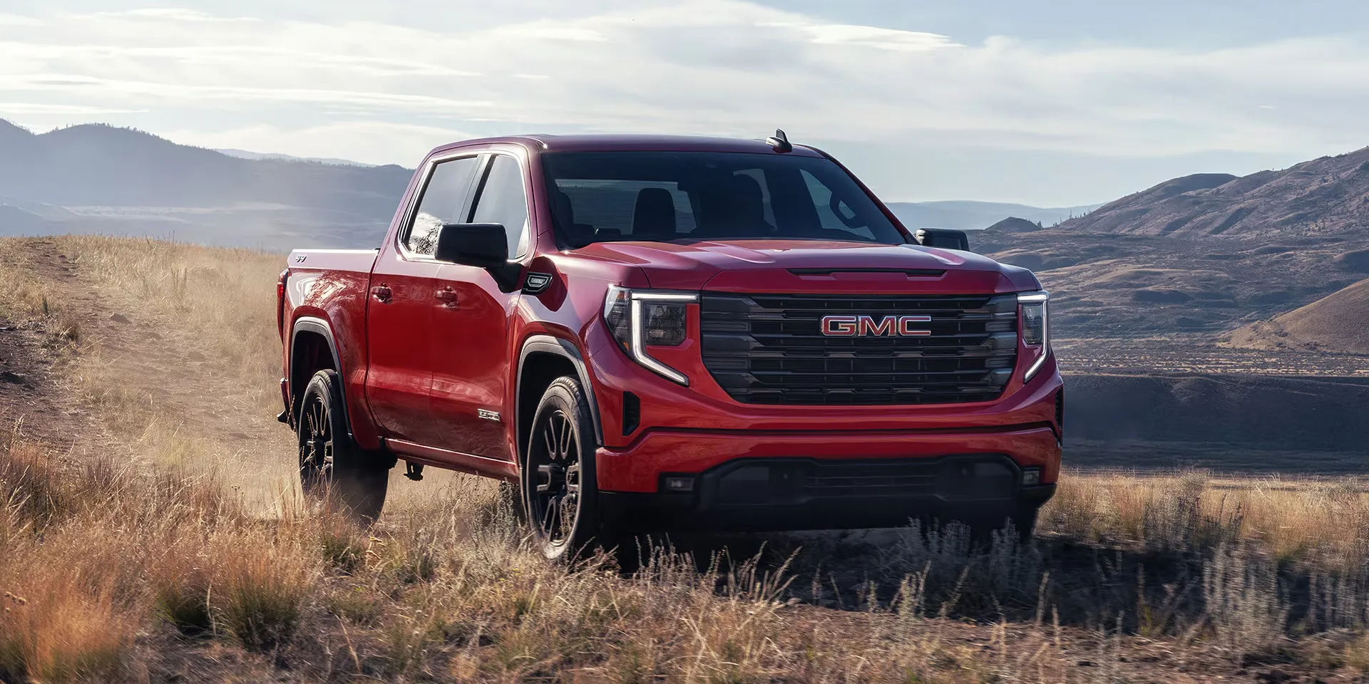 GMC Sierra 1500 2026 rouge sur un sentier en r&eacute;gion montagneuse.