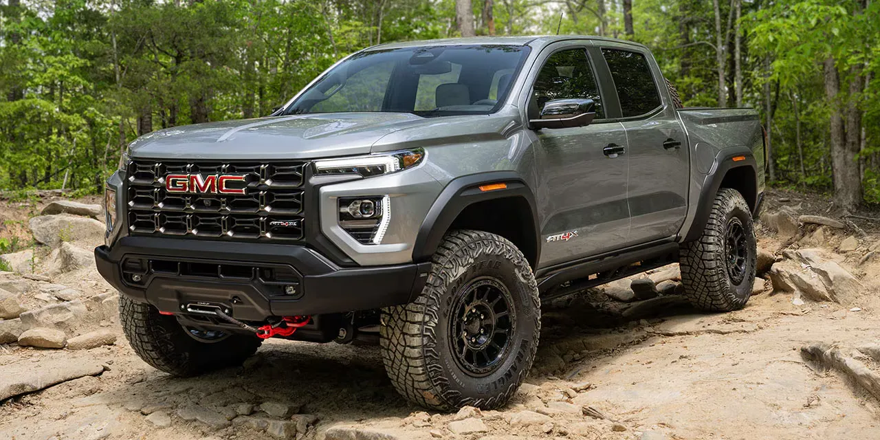 GMC Canyon AT4X 2026 gris sur un sentier rocheux en for&ecirc;t.