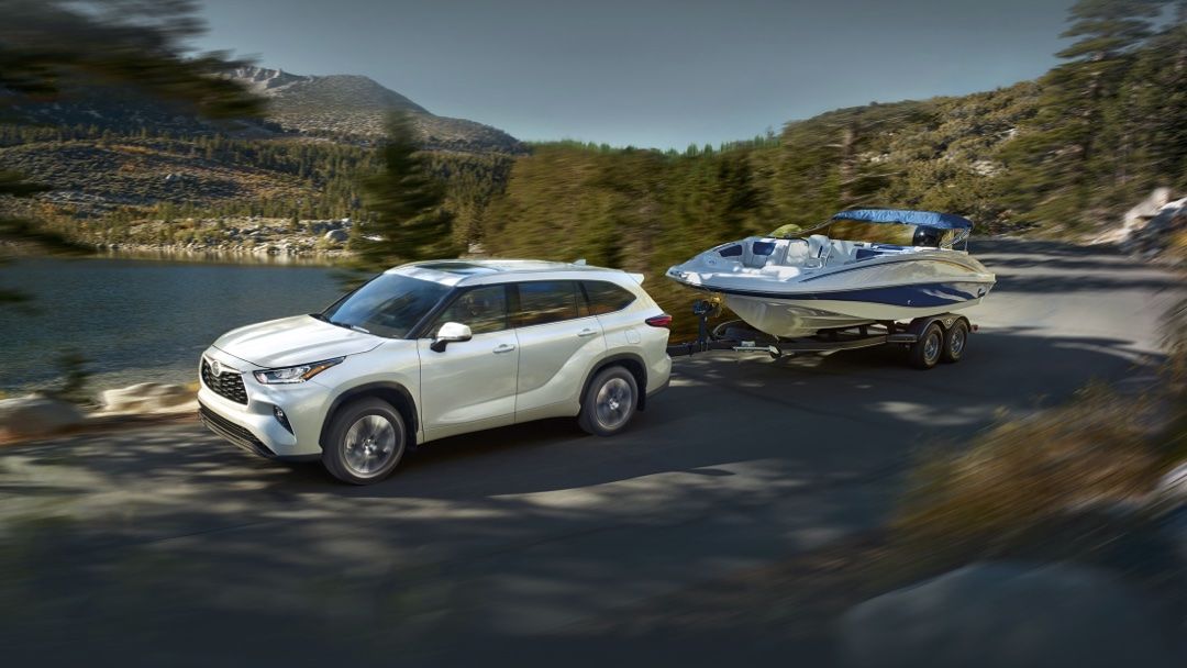 Le Toyota Highlander 2024 qui tire un bateau sur une route au bord de l'eau.