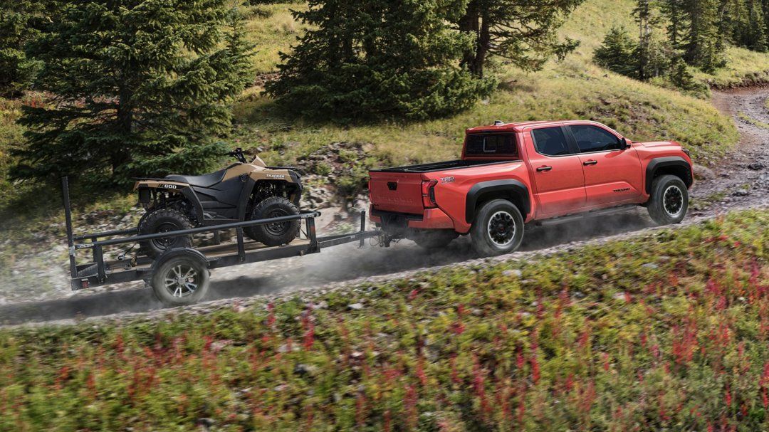 A Toyota Tacoma towing a quad on a trailer on a gravel road.