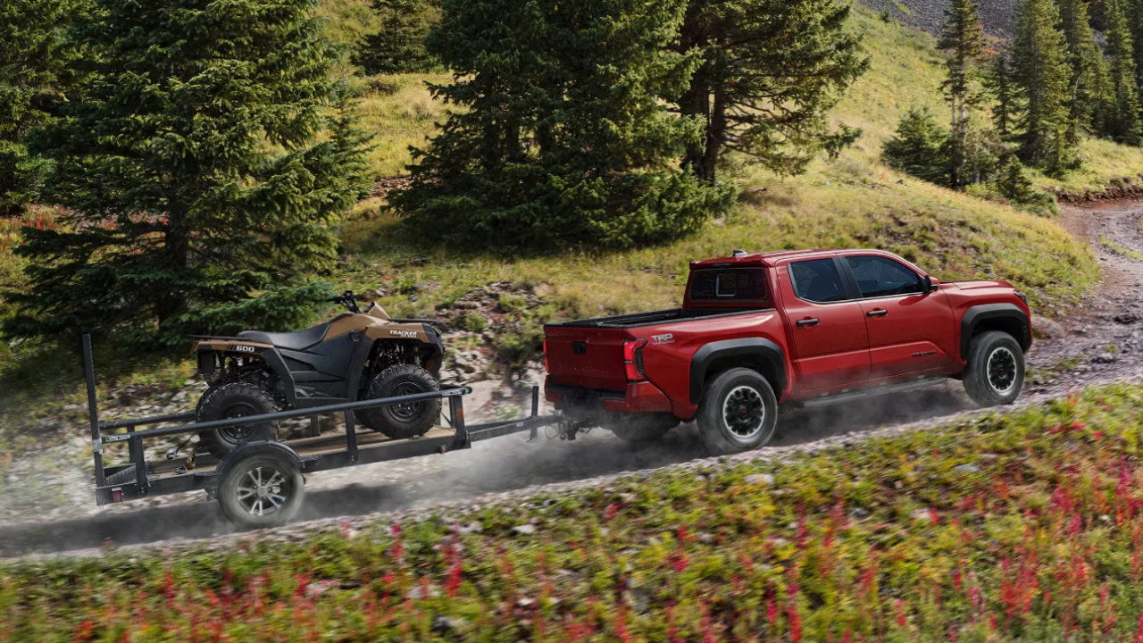 rear side view of a 2025 Toyota Tacoma towing an ATV on a country road