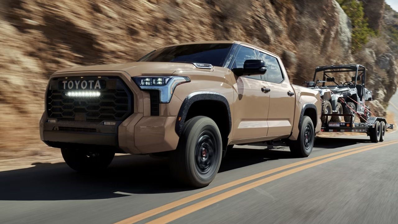 vue latérale avant d'un Toyota Tundra 2025 qui remorque un side by side sur une route de campagne