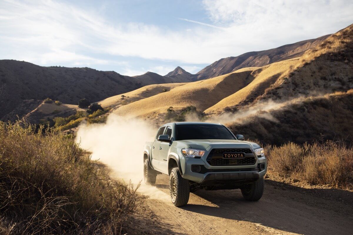 Front 3/4 view of a 2022 Toyota Tacoma Trail truck driving on a dirt road in nature