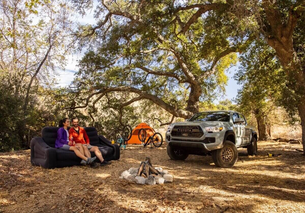 A couple and their 2022 Toyota Tacoma Trail truck sit outdoors by a campfire