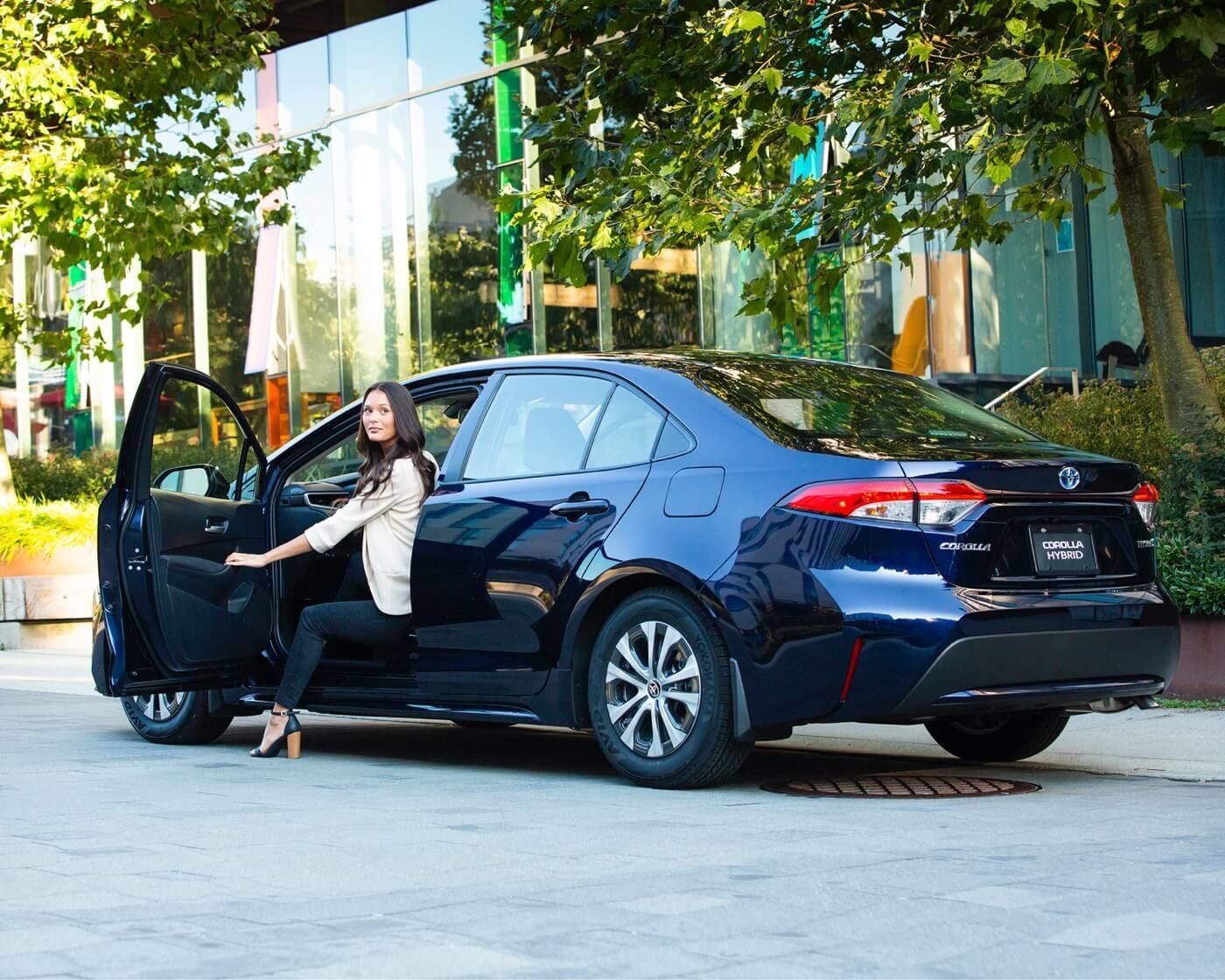 Vue latérale 3/4 arrière d'une Toyota Corolla Hybride 2022 avec une femme sortant du véhicule
