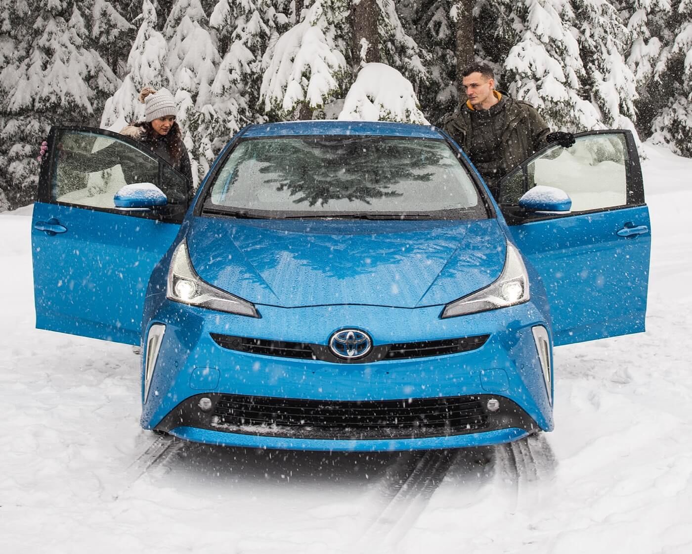 Vue avant d'une berline hybride Toyota Prius 2022 bleue avec un couple embarquant dans le véhicule sous la neige