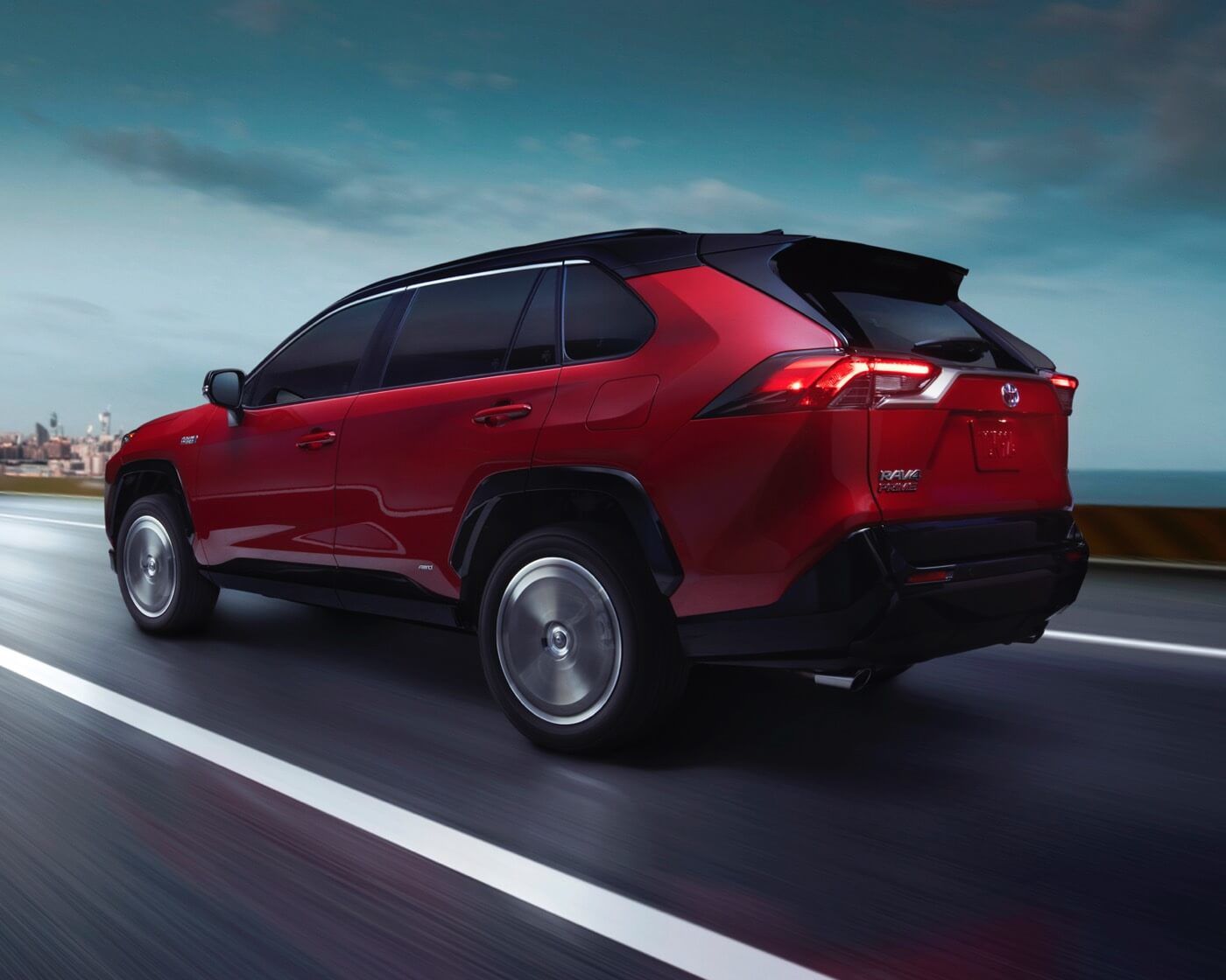Rear 3/4 side view of a red 2022 Toyota RAV4 Prime SUV driving on a road