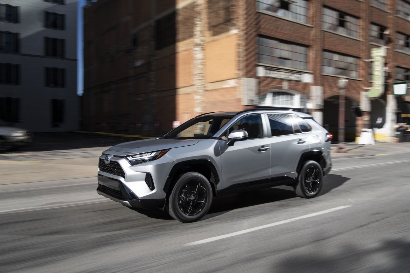 Front 3/4 side view of a silver 2022 Toyota RAV4 SE Hybrid SUV driving on a city boulevard