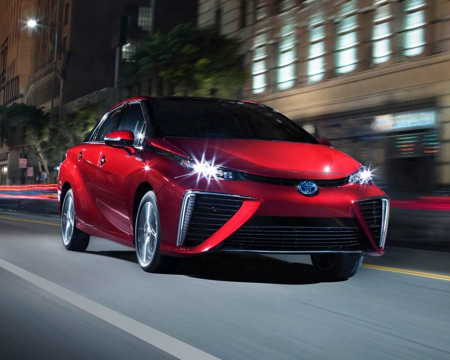 Front 3/4 view of a red 2020 Toyota Mirai hydrogen car being driven on a city boulevard