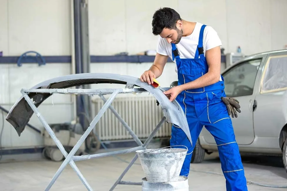 A mechanic sands a car bumper in a repair shop - Oakville Toyota Collision Centre