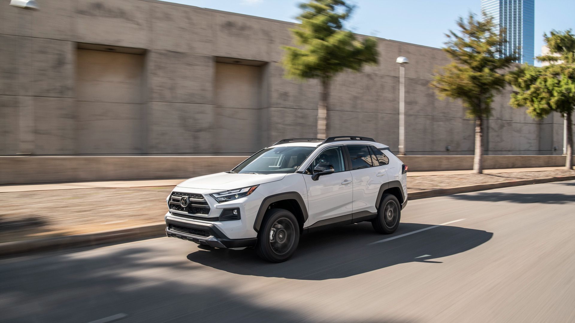 Toyota RAV4 - A white Toyota RAV4 driving on a city street with modern buildings in the background - AutoPark Brampton - Used car dealership in Brampton, Ontario