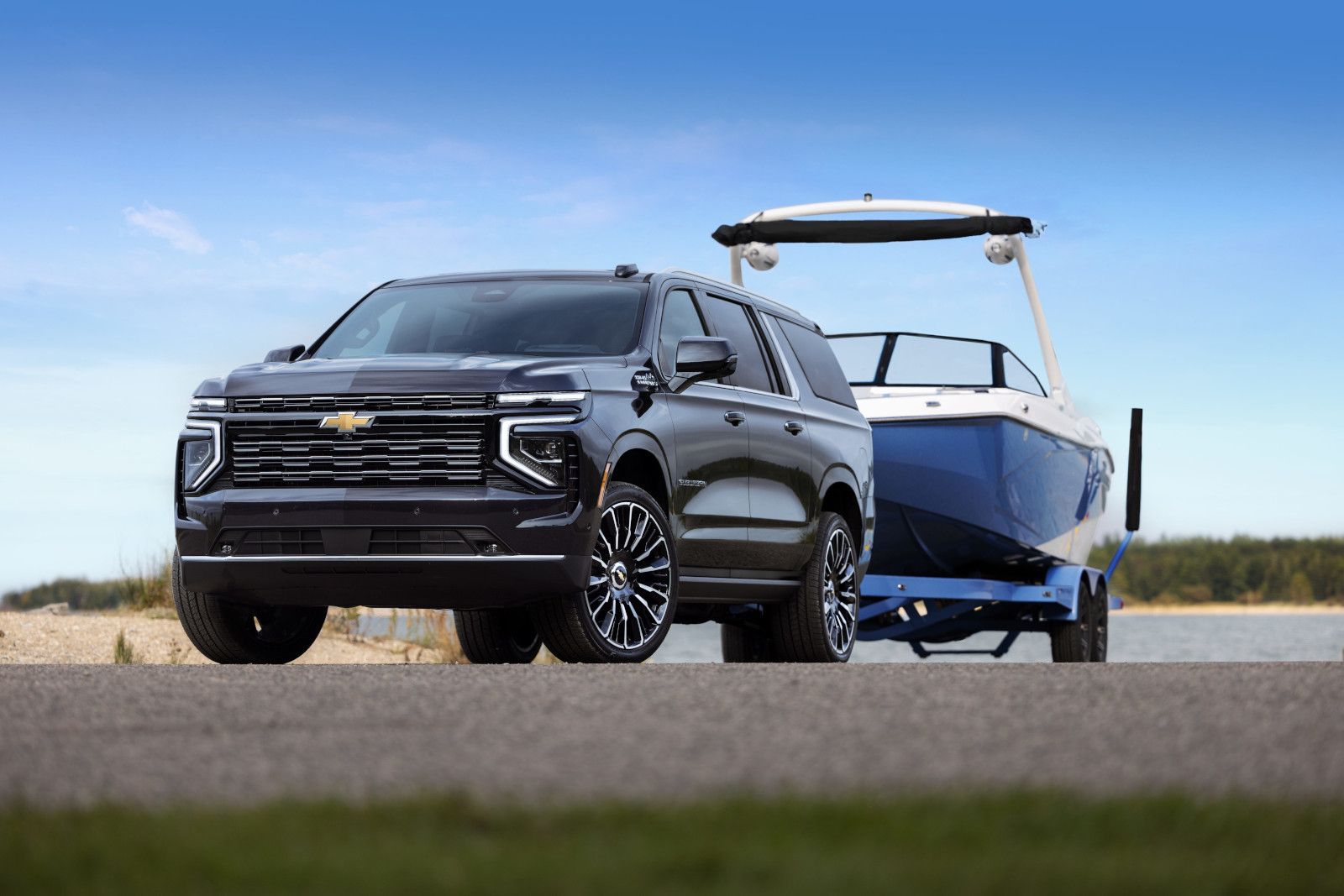 2026 Chevrolet Suburban - a black Chevrolet Suburban towing a blue boat near a lake - Applewood Auto - New car dealership in Mississauga, Ontario
