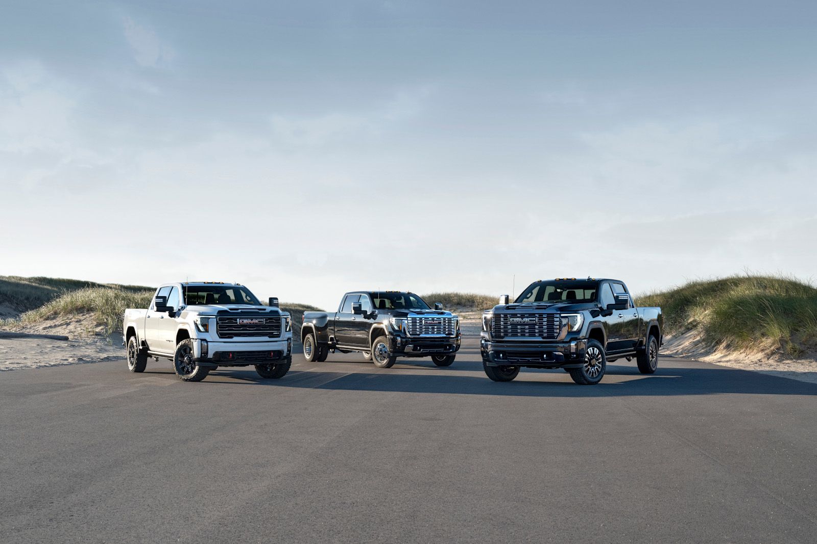 2026 GMC Sierra HD - a lineup of three 2026 GMC Sierra HD trucks including Denali and Dually models parked on a road near sand dunes - Applewood Chevrolet, Buick, GMC - Used car dealership in Mississauga, Ontario
