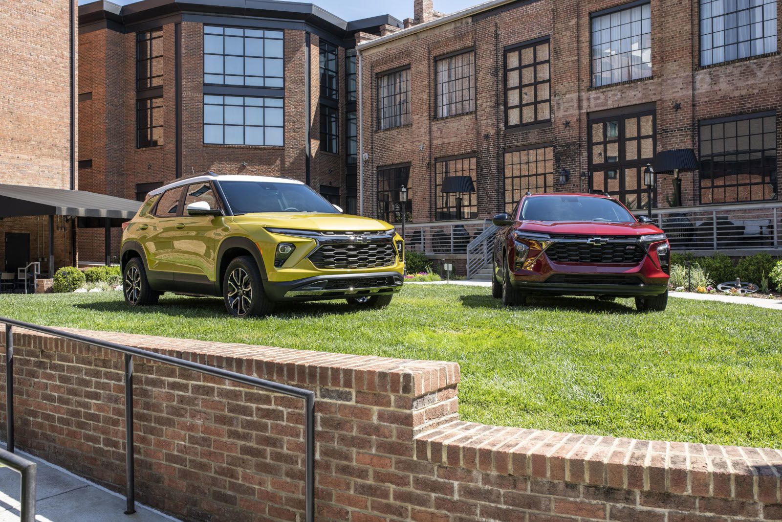 2026 Chevrolet Trax and Trailblazer - a yellow Chevrolet Trailblazer and a red Chevrolet Trax parked on a grassy courtyard in front of a brick building - City Chevrolet, Buick, GMC - New car dealership in Toronto, Ontario