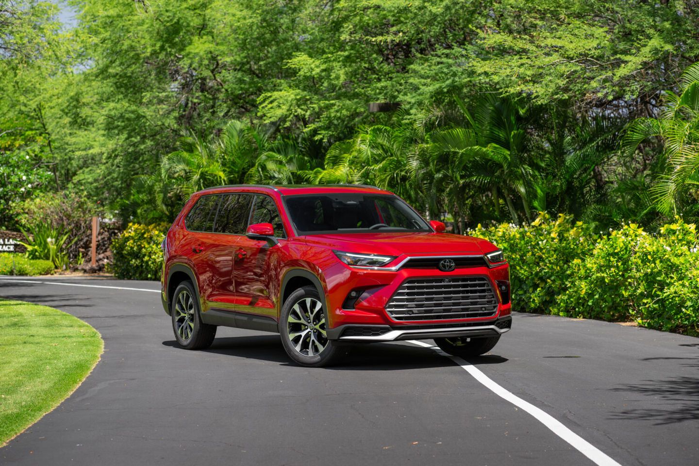 2026 Toyota Grand Highlander - A red 2026 Toyota Grand Highlander parked on a paved road surrounded by lush green trees - Georgetown Toyota - Toyota car dealership in Georgetown, Ontario
