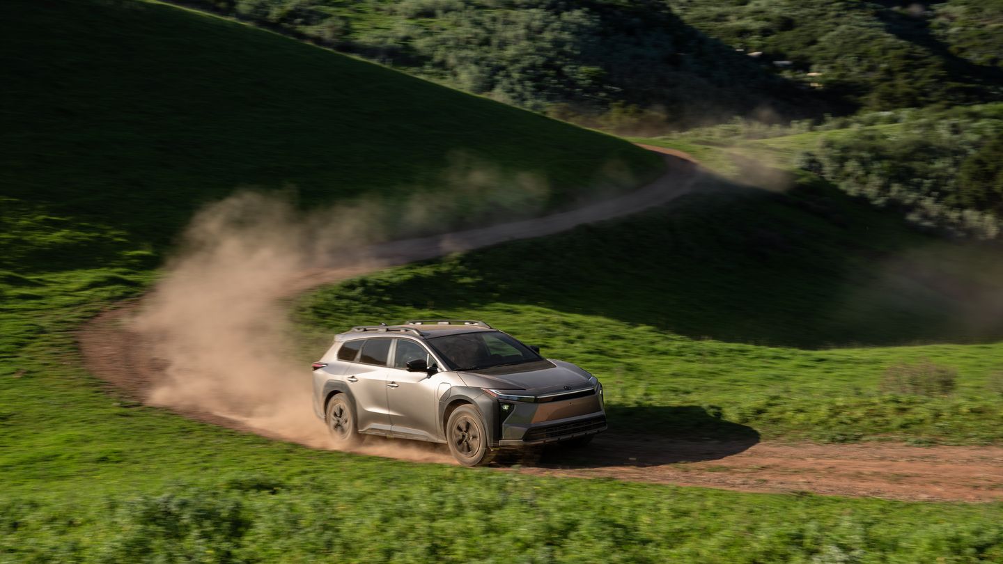 2026 Toyota bZ Woodland - a bronze 2026 Toyota bZ Woodland kicking up dust while driving along a winding dirt path in a green valley - Georgetown Toyota - Toyota new car dealership in Georgetown, Ontario