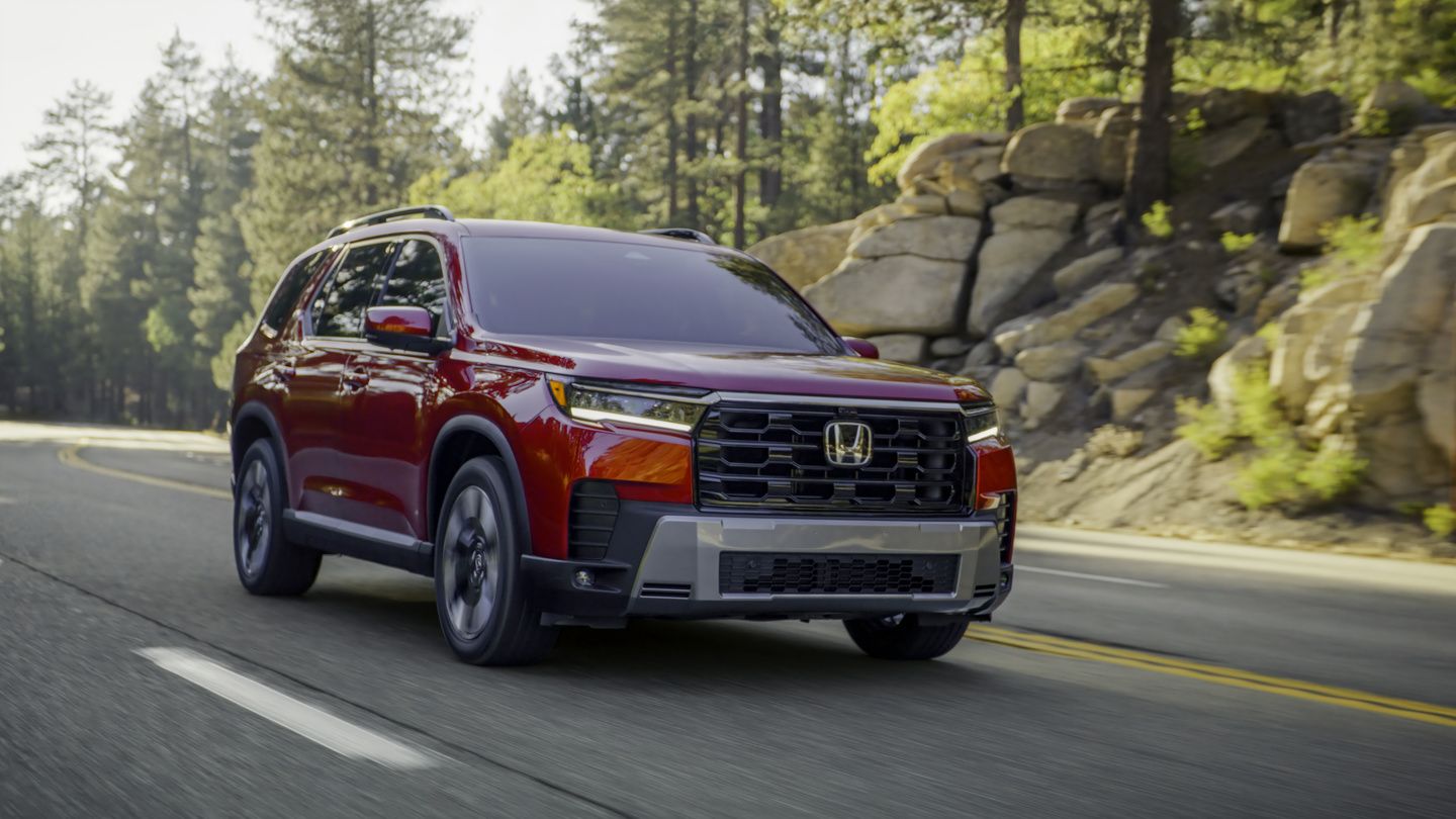 2026 Honda Pilot Touring - Front three-quarter view of a red 2026 Honda Pilot Touring driving down a scenic mountain road - Orangeville Honda - New car dealership in Orangeville, Ontario