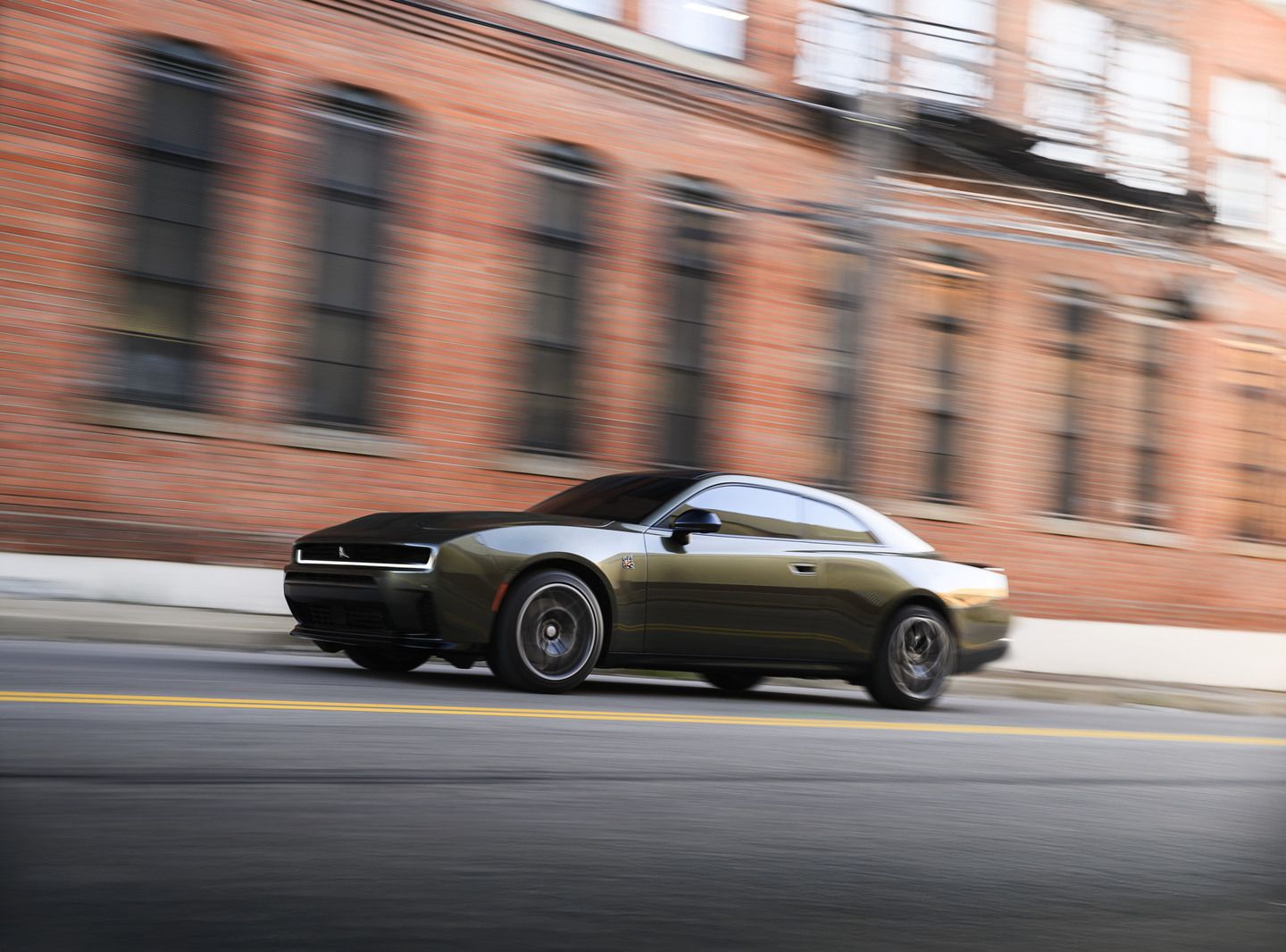 2026 Dodge Charger - side profile view of a green 2026 Dodge Charger driving fast past a brick building - Cooksville Dodge - New car dealership in Mississauga, Ontario
