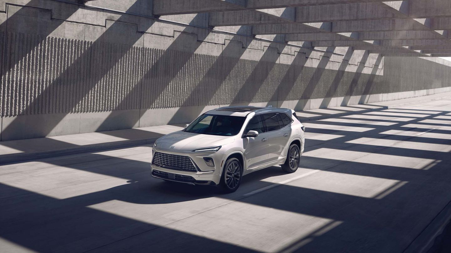 2026 Buick Enclave - Front three-quarter view of a white 2026 Buick Enclave driving through an overpass with stark concrete structures and shadow patterns - City Chevrolet, Buick, GMC - Buick new car dealership in Toronto, Ontario