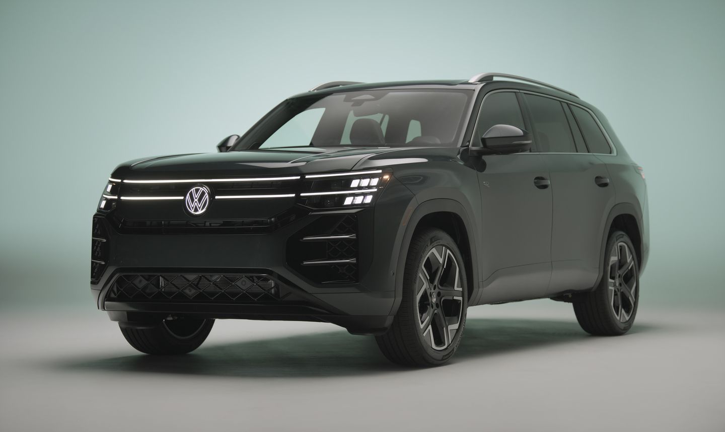 2027 Volkswagen Atlas - front three-quarter studio view of a dark green Atlas with illuminated front grille and headlights - Humberview Volkswagen - New car dealership in Toronto, Ontario