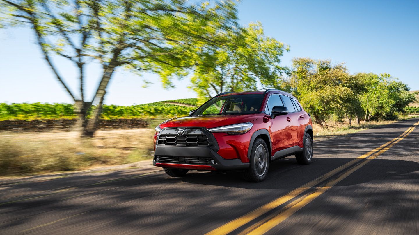 2026 Toyota Corolla Cross - a red 2026 Toyota Corolla Cross driving down a paved countryside road - Humberview Group - New car dealerships in Ontario