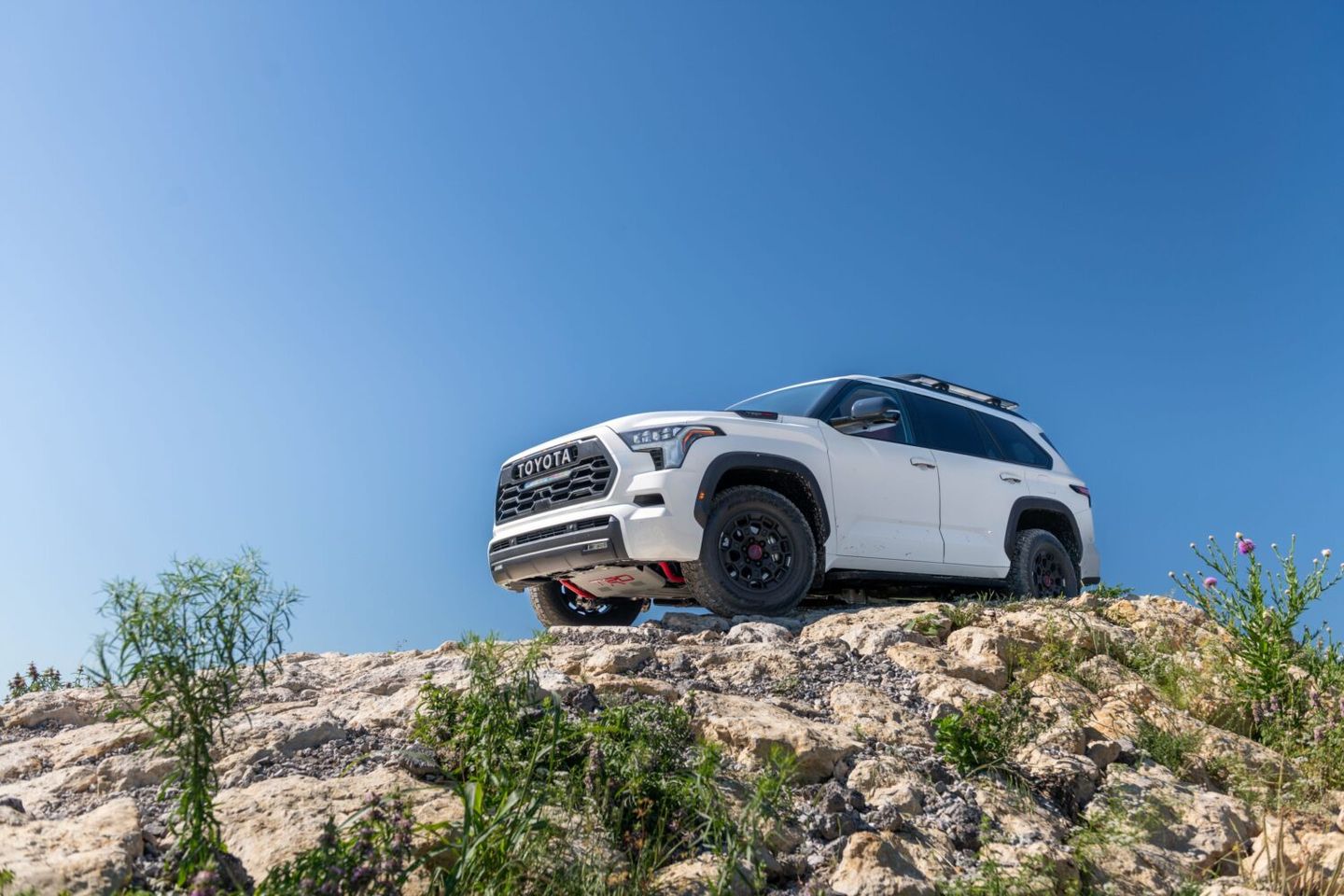 2026 Toyota Sequoia - A low-angle shot of a white 2026 Toyota Sequoia TRD Pro parked on a rocky hill under a clear blue sky - Orangeville Toyota - Toyota car dealership in Orangeville, Ontario