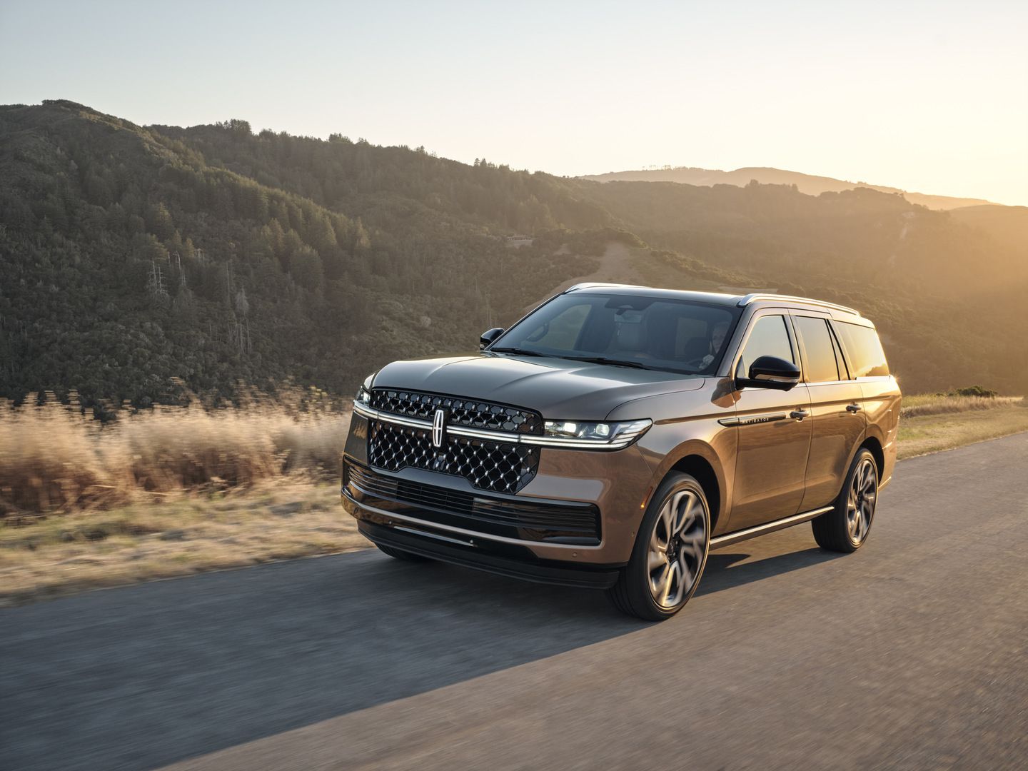2026 Lincoln Navigator - a three-quarter front view of a 2026 Lincoln Navigator driving on a winding road with a view of a grassy hill in the background - Bayfield Lincoln - Lincoln car dealership in Barrie, Ontario