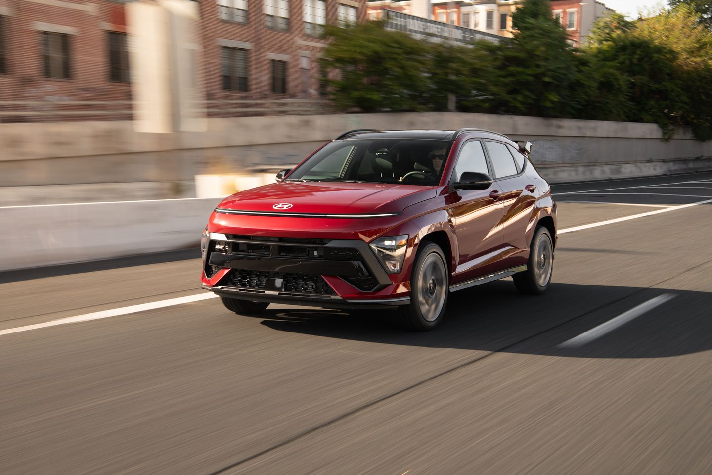 2027 Hyundai Kona N Line - front three-quarter view of a red 2027 Hyundai Kona N Line driving on the highway - Woodstock Hyundai - Hyundai new car dealership in Woodstock, Ontario