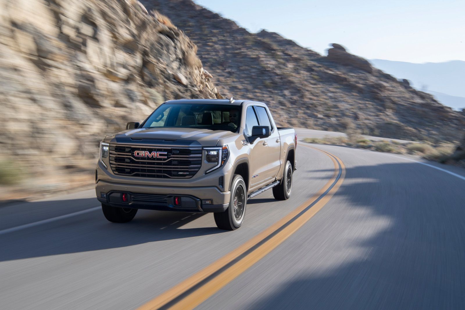 2026 GMC Sierra - a tan 2026 GMC Sierra driving on a winding paved mountain road - Applewood Chevrolet, Buick, GMC - GMC car dealership in Mississauga, Ontario