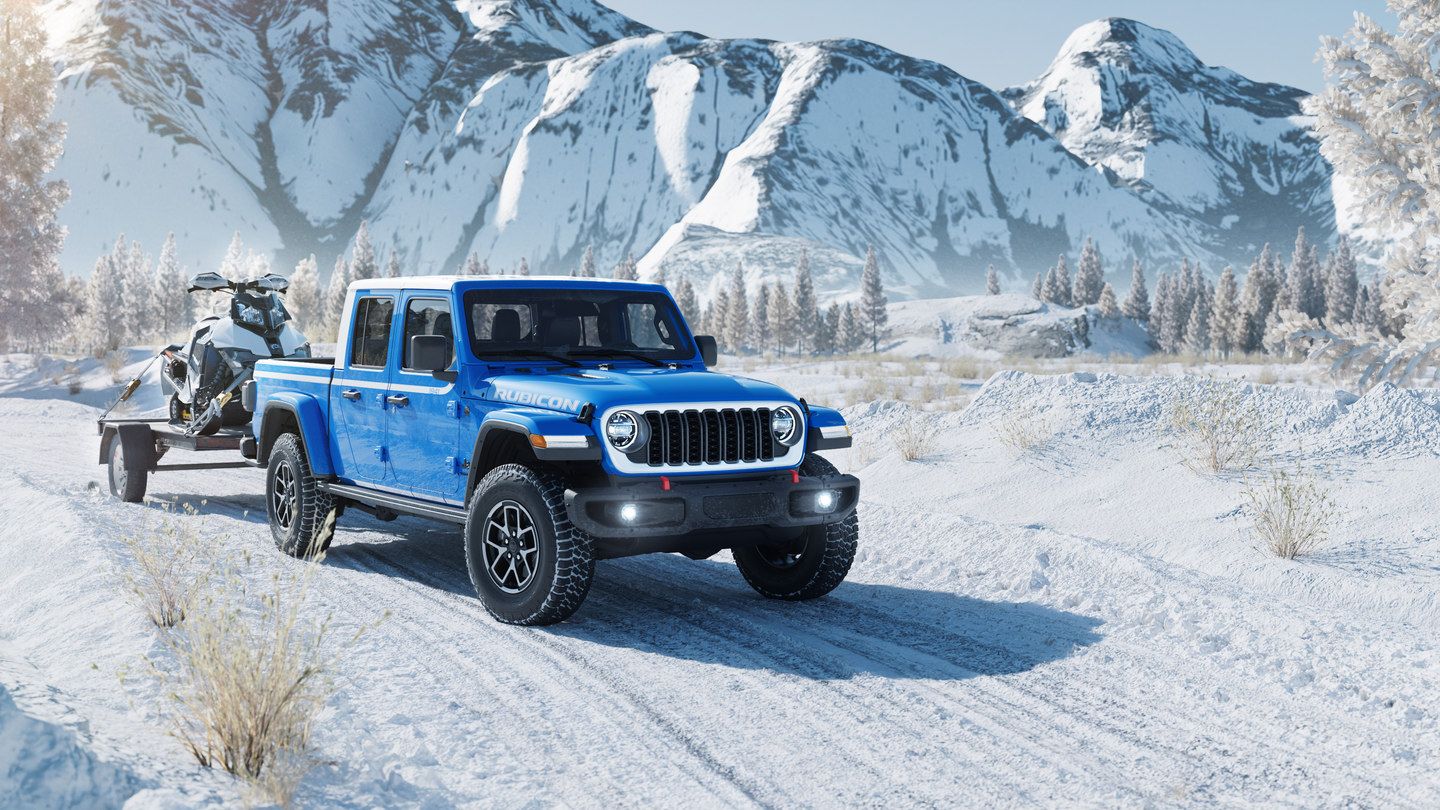 2027 Jeep Gladiator - a blue 2027 Jeep Gladiator towing a snowmobile on a snowy road - Cooksville Chrysler, Jeep, Dodge, Ram - New car dealership in Mississauga, Ontario