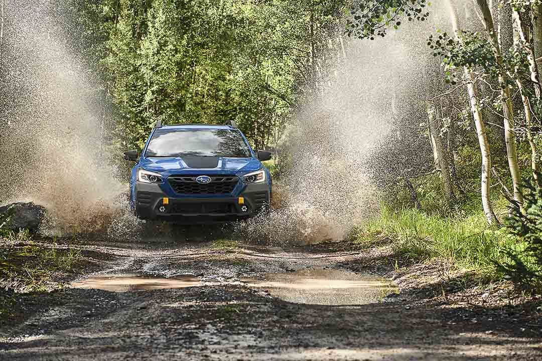 Le Subaru Outback Wilderness 2022 éclaboussant l'eau en roulant sur une terre humide