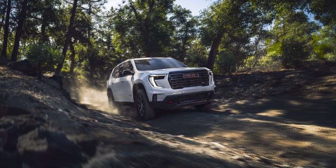 Vue 3/4 avant du GMC Acadia 2025 roulant sur un chemin en forêt.