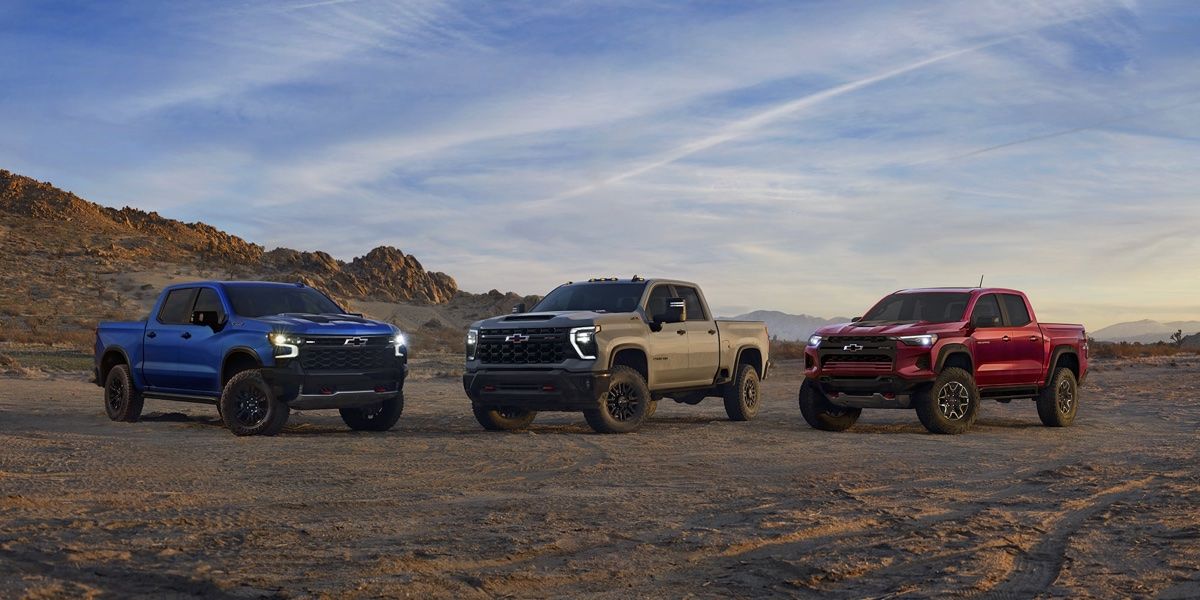 3 Pickups Chevrolet stationné sur un chemin de terre.