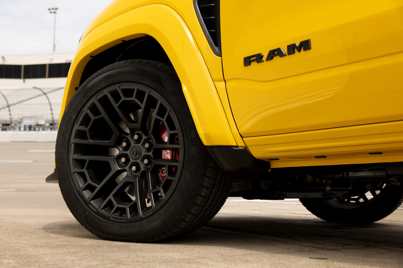 Close-up of the black alloy wheel and red brake caliper on the yellow 2027 Ram 1500 Rumble Bee.