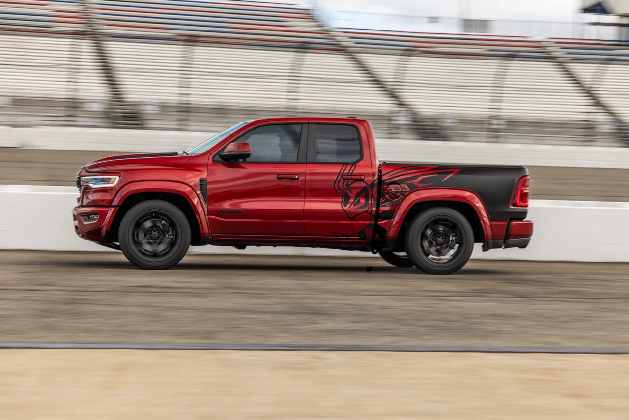 Red Ram 1500 Rumble Bee driving on a racetrack, shown in profile with bee graphics along the rear doors and bed.
