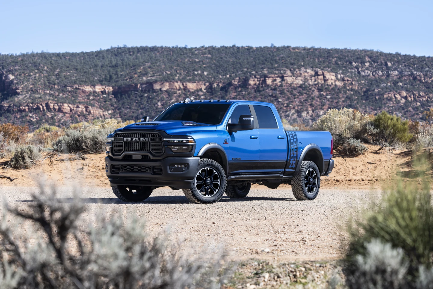 Blue 2027 Ram 2500 Power Wagon with black wheels and off-road tires, parked in a rocky landscape.