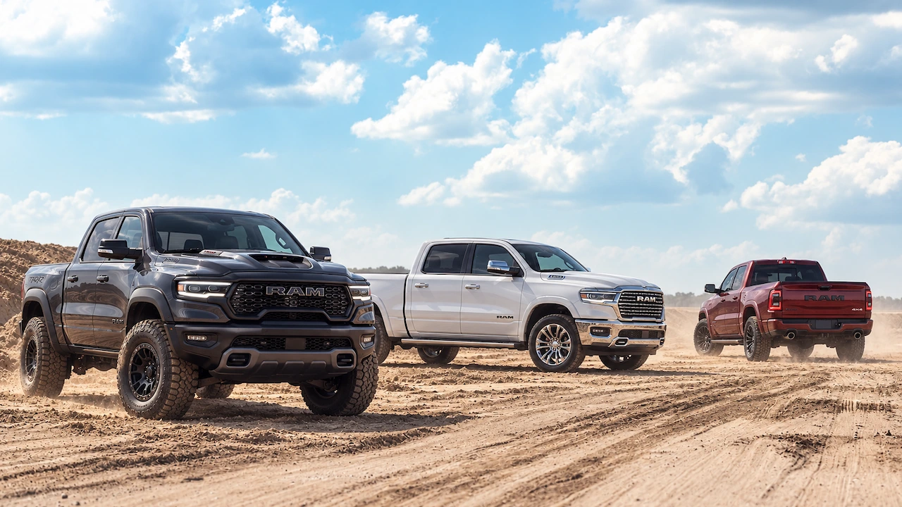Three Ram 1500 pickups in different trims, shown in grey, white and red on sandy terrain.