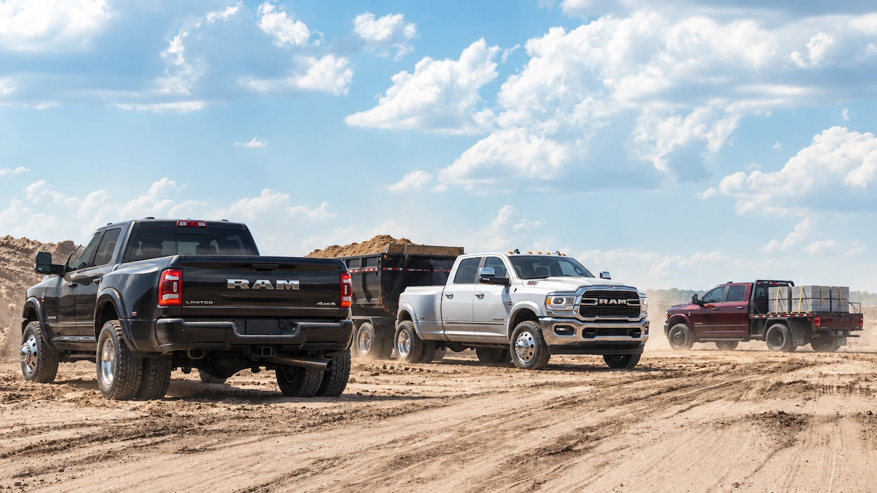 Ram 3500 lineup with a black dually pickup, a white pickup towing a dump trailer and a red flatbed work truck.
