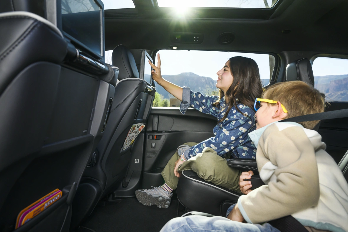 Two children seated in the rear cabin of a 2027 Chrysler Pacifica with a panoramic sunroof.