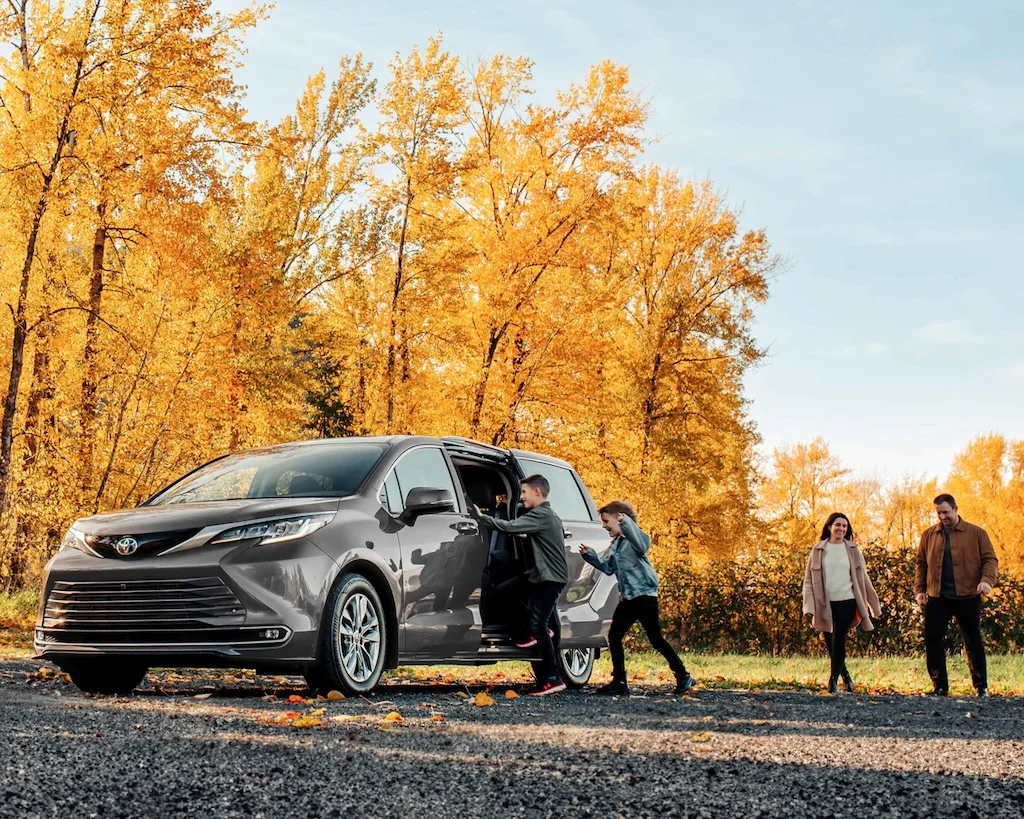 Grey 2026 Toyota Sienna parked beside a family among autumn trees.