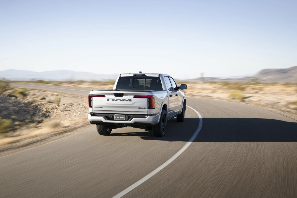 Rear view of a white Ram 1500 REV driving along a winding road through a dry open landscape.